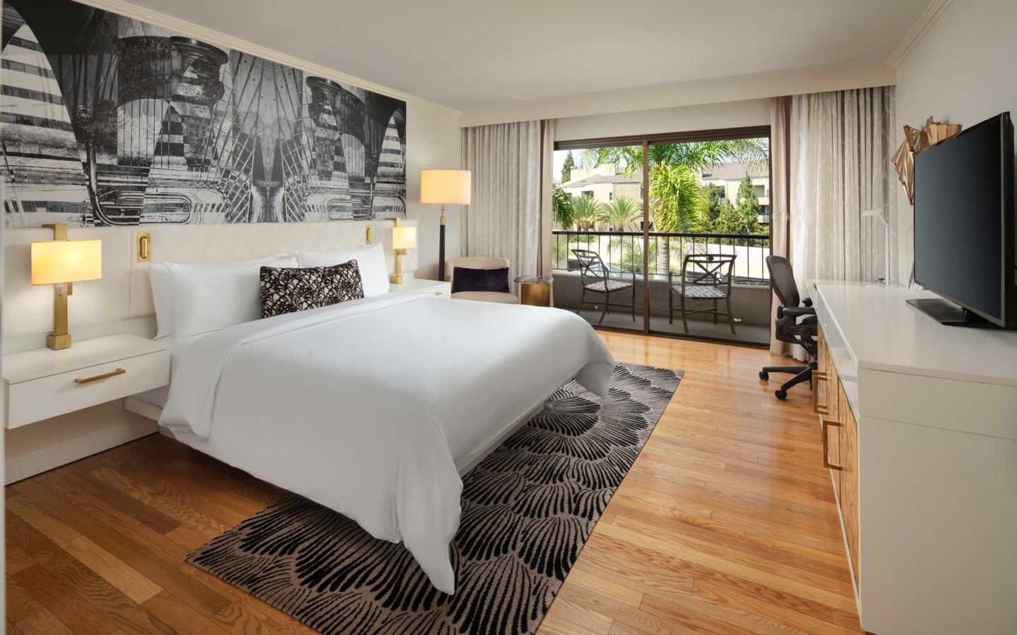 modern luxury hotel room with hardwood floors king bed tv desk and balcony