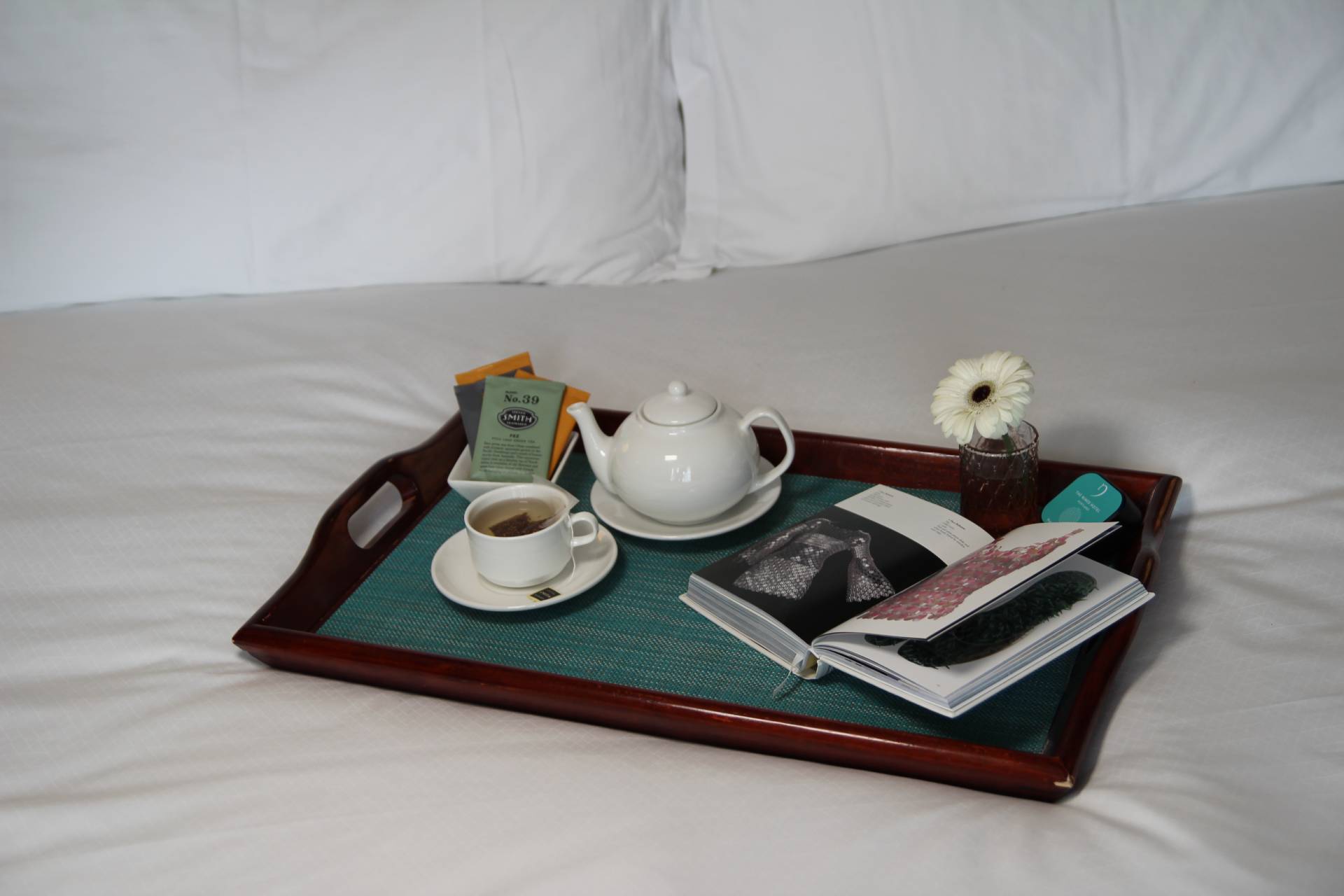 a tray with a pot of tea and a cup and saucer on a bed