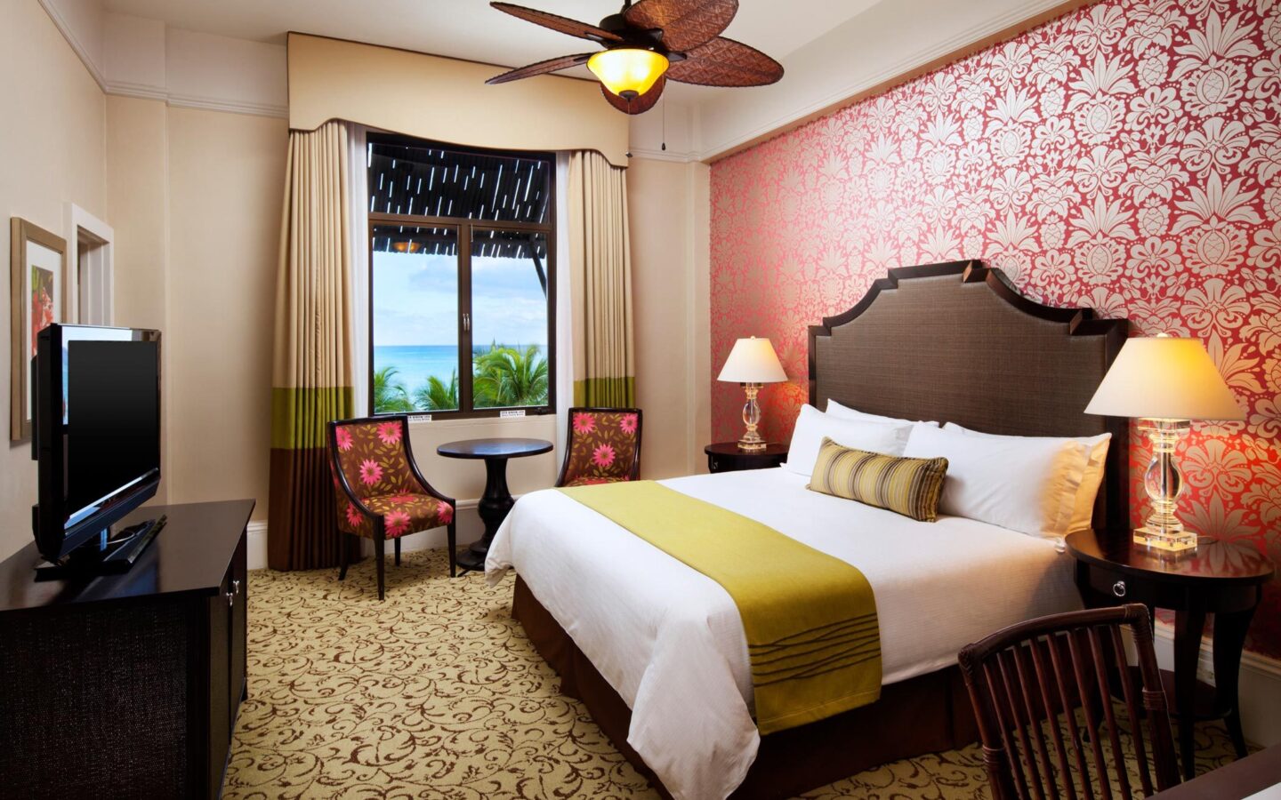 hotel room with king bed, pink and white flowered wallpaper, and ocean view window
