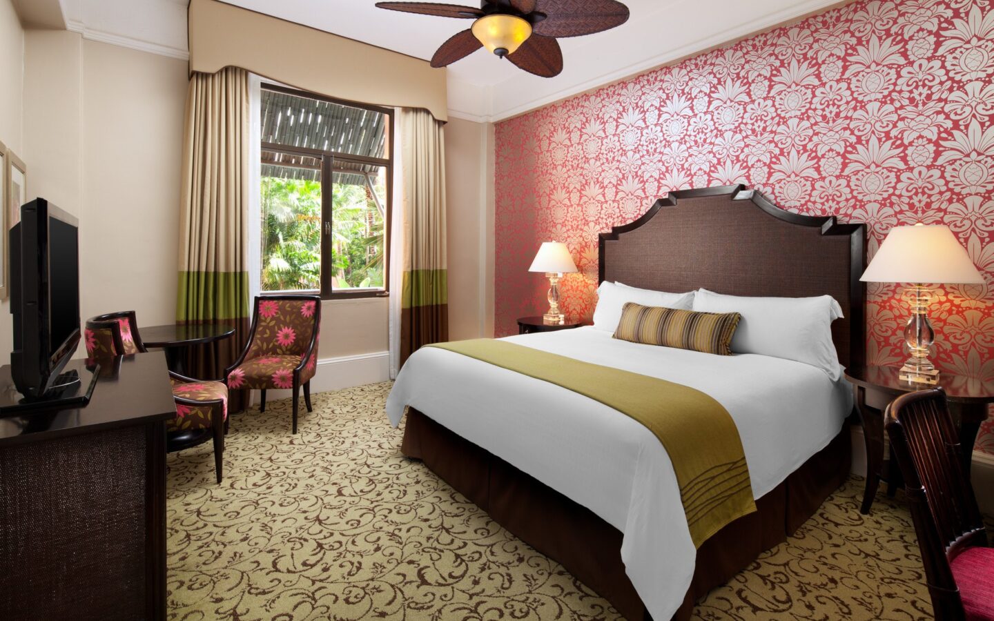 hotel room with king bed, red and white flowered wallpaper and garden view window