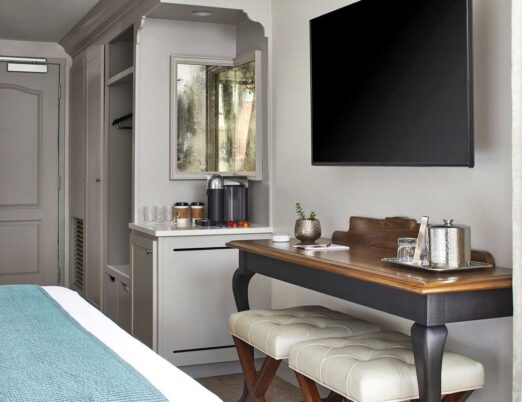 a bright luxury hotel room with a king-size bed with white linens, a chandelier, a plush day bed, and a flat screen tv