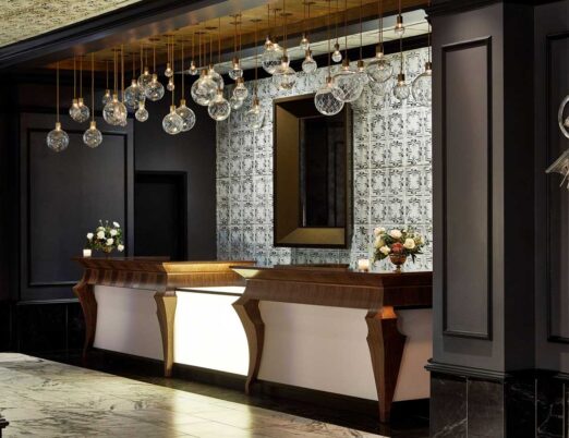 dark hotel lobby front desk with gold accents, a white fireplace, large mirror, and large glass light fixture