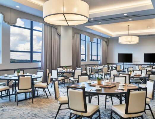 boardroom with large windows full of round tables surrounded with chairs, with two large flat screen TVs at the front of the room
