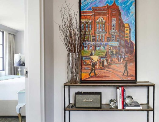 bright hotel room entrance with a table displaying a vase, radio, and large, brightly coloured painting