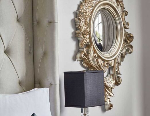 bright hotel room side table with a black table lamp on it and a gold mirror next to it