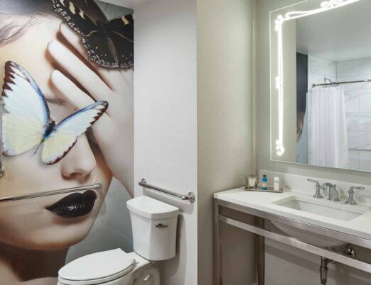 a hotel bathroom with a full wall art piece featuring a woman's face and a butterfly