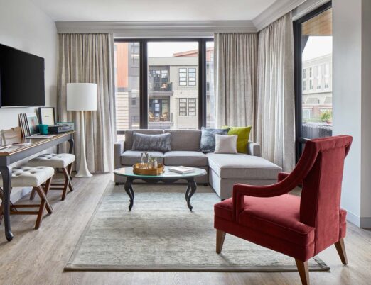 Luxury hotel living room suite with a sectional sofa, red plush chair, flat screen tv, and large windows