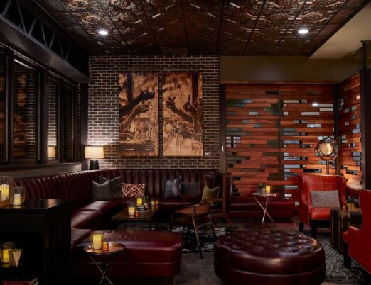 dark leather booth with an ottoman and candles surrounding it, with brown brick walls with brown artwork on them