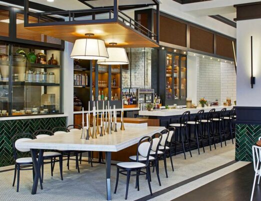 bright restaurant with white curtains, white chairs, and wooden tables with glasses and flowers on them
