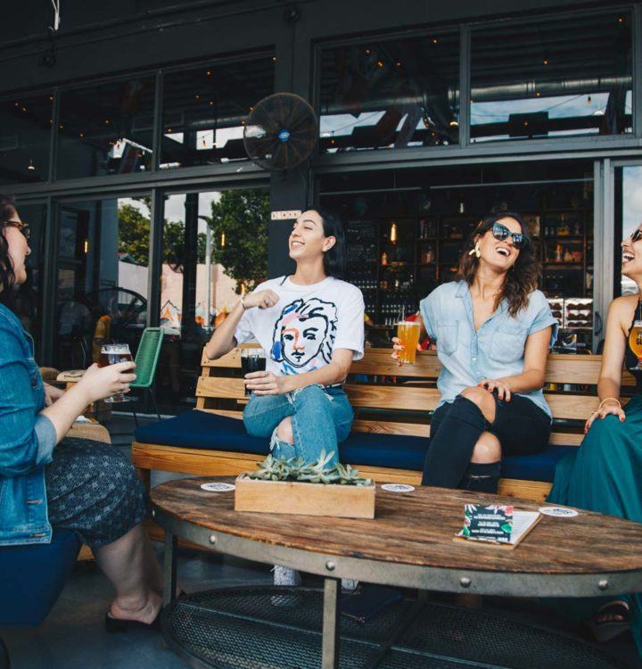 a group of friends sitting outside of a restaurant drinking beer