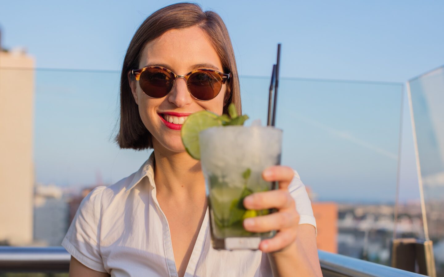 woman in white shirt holding up a mojito drink