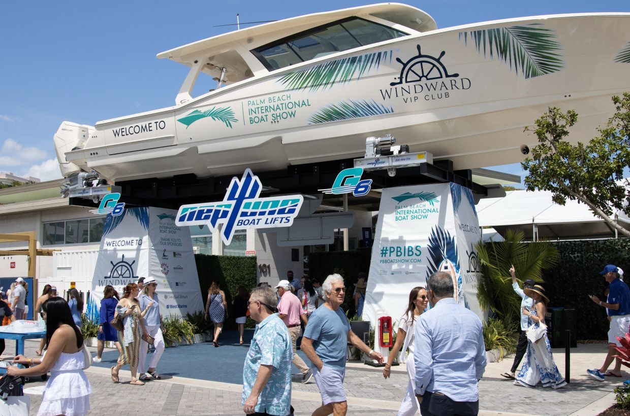 Entrance to the Palm Beach International Boat Show with a large boat displayed overhead and attendees walking below.