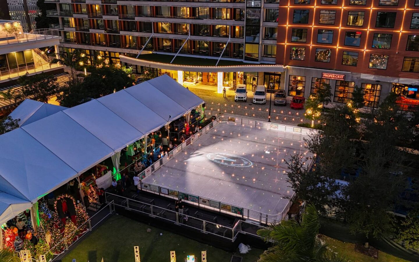 Outdoor ice skating rink and covered holiday market illuminated at night in an urban plaza.