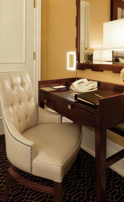 tufted white padded armchair sitting under the working desk within guest room