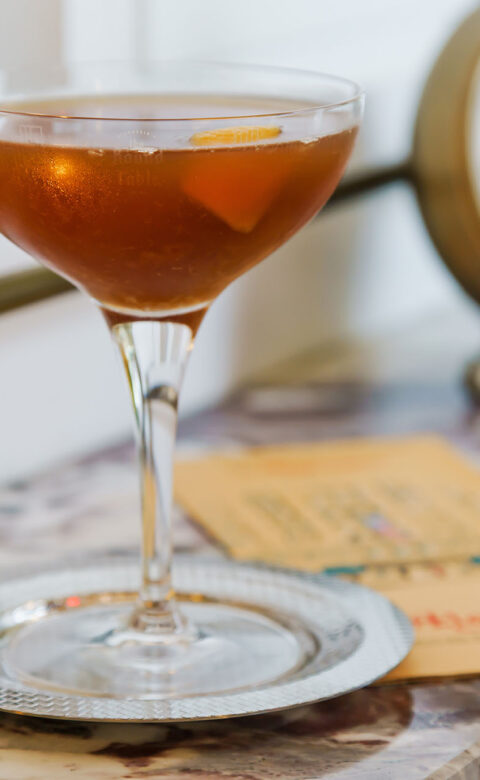 a cocktail in a stemmed cocktail glass with a slice of orange peel