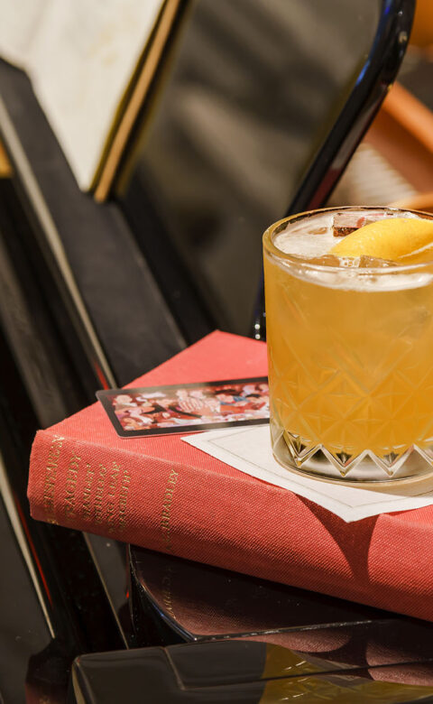 a cocktail in a cocktail glass on top of an antique book resting on a piano