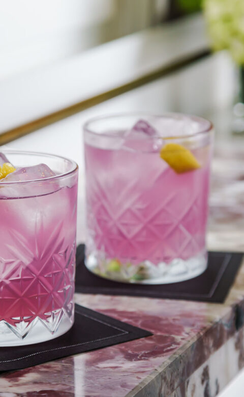 two purple cocktails in crystal rocks glasses