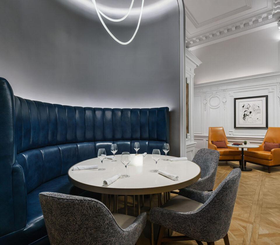 a round dining table in a hotel dining room with 3 chairs and high-backed blue leather booth seat