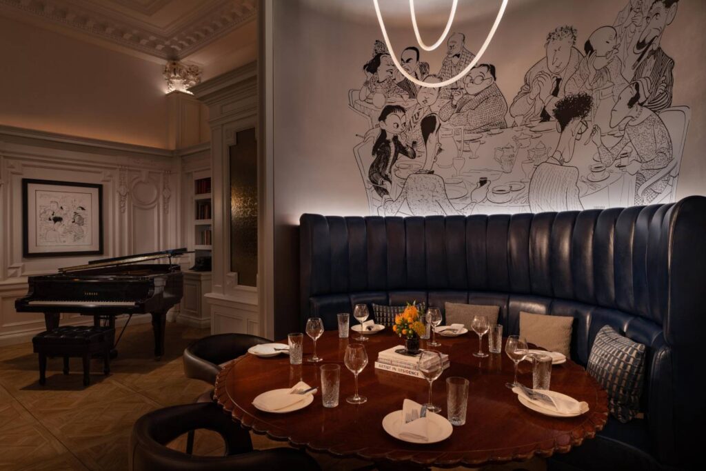 Elegant restaurant dining alcove with curved blue banquette seating, a set table, statement lighting and illustrated wall art.