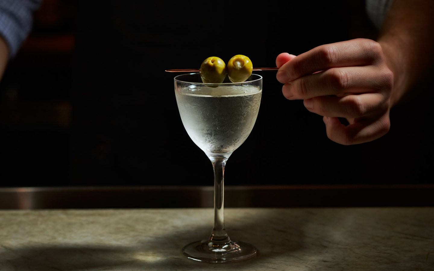 cocktail in long stemmed glass garnished with two olives