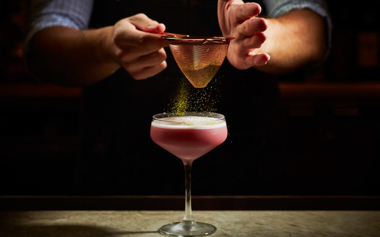 clear cocktail glass and bartender adding sprinkled garnish