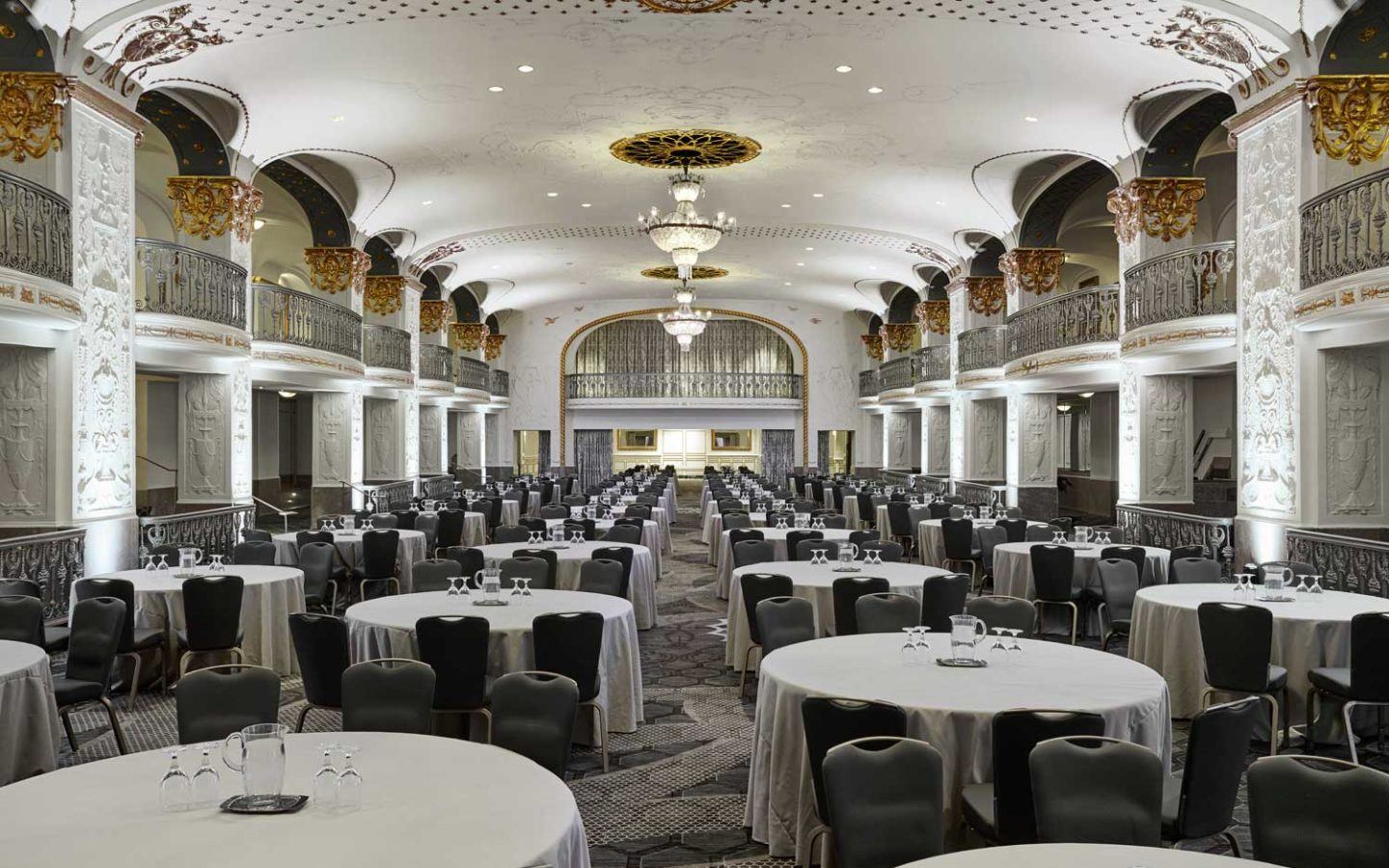 a ballroom filled with round dining tables covered in table clothes prepared for event