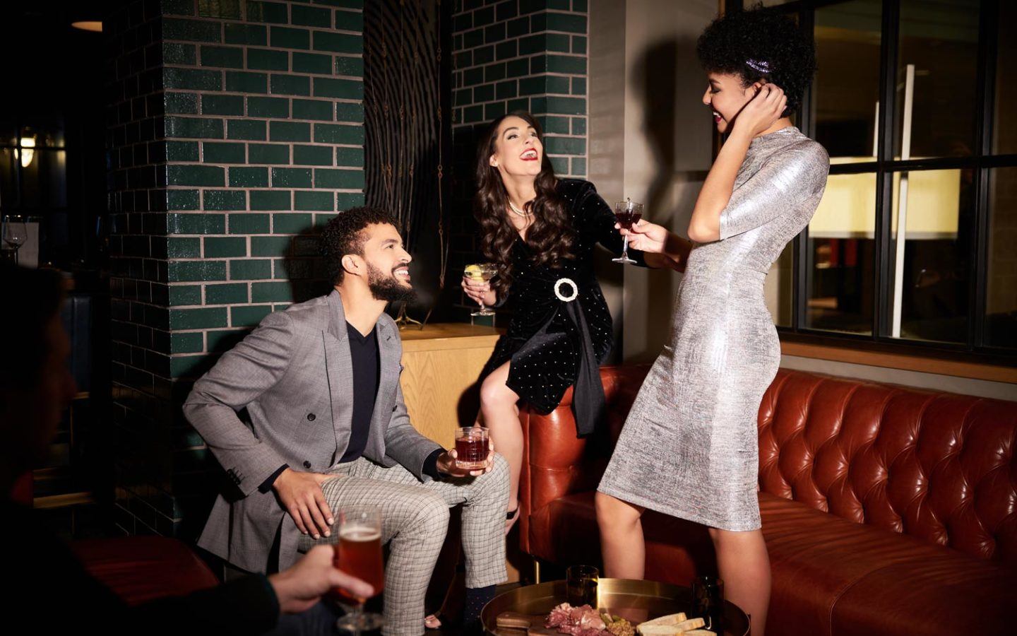 three people with cocktails socializing on a red leather couch in a lounge