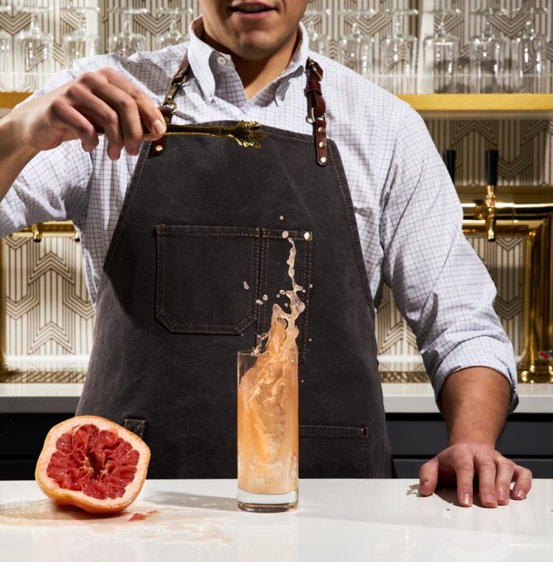 bartender making a drink at a bar next to a squeezed grapefruit