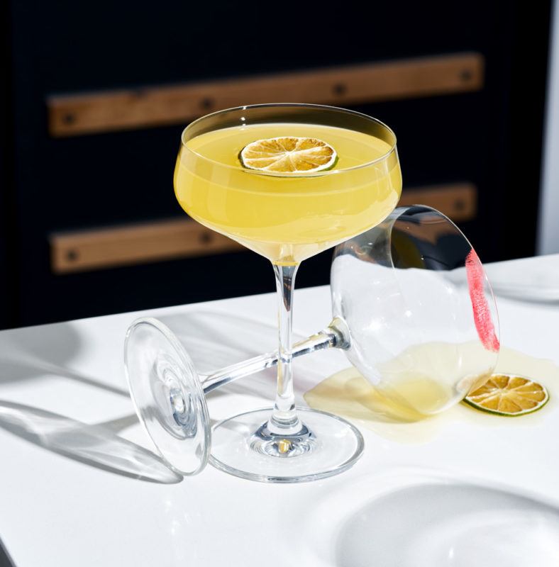 clear glass with a cocktail next to a glass that's tipped over with a red lipstick stain on it