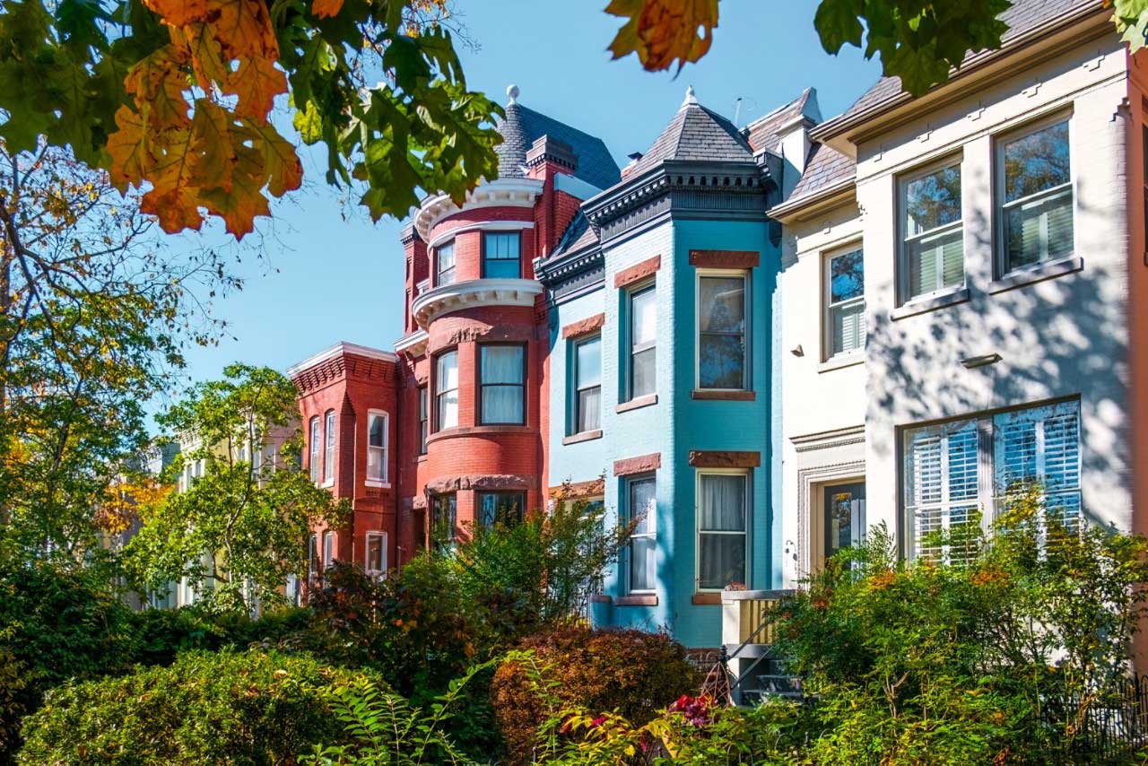 a row of multi - colored houses with trees in the foreground