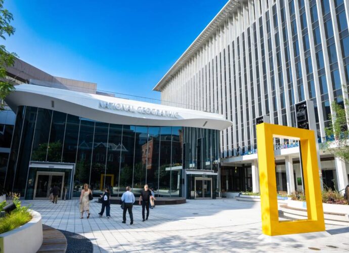 National Geographic Museum exterior with a large yellow frame sculpture, glass entrance, and visitors walking through the plaza.