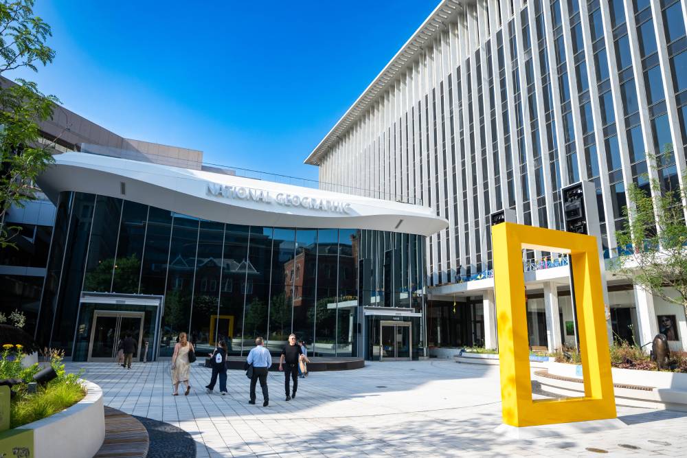National Geographic Museum exterior with a large yellow frame sculpture, glass entrance, and visitors walking through the plaza.