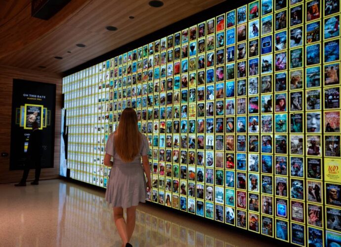 Visitor walking past a wall of National Geographic magazine covers in a museum exhibit.