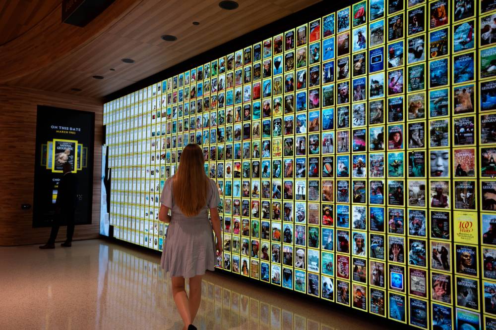 Visitor walking past a wall of National Geographic magazine covers in a museum exhibit.