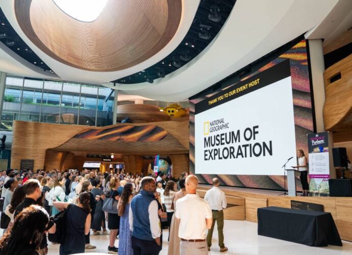 Crowd gathered inside the National Geographic Museum of Exploration during an event presentation in a large atrium.