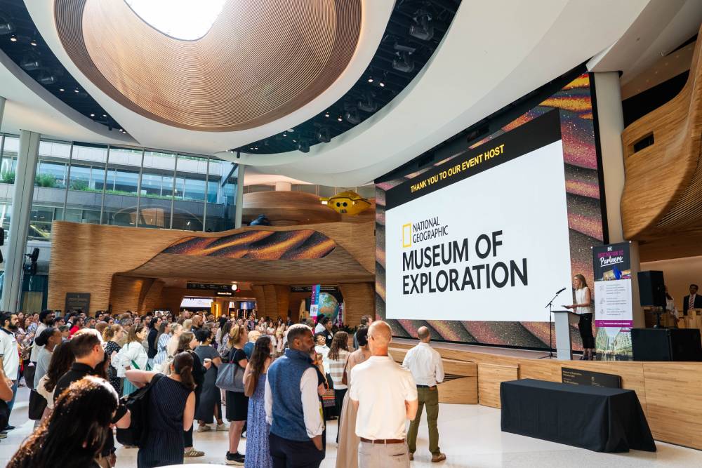 Crowd gathered inside the National Geographic Museum of Exploration during an event presentation in a large atrium.