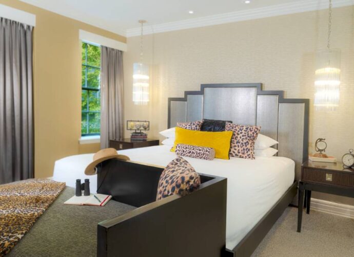 Hotel bedroom with a king bed, leopard-print accents, yellow pillows, pendant lights, and grey curtains.