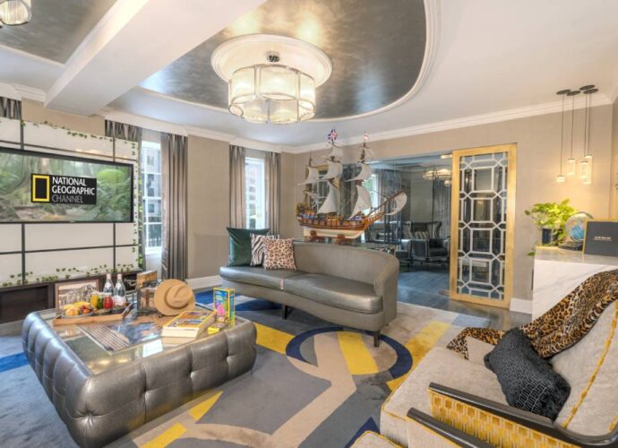 National Geographic themed hotel suite with a living area, ship model, patterned decor, and a television displaying the National Geographic Channel logo.