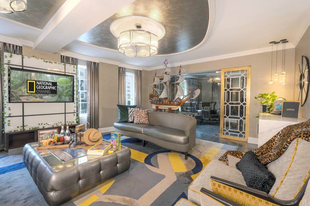 National Geographic themed hotel suite with a living area, ship model, patterned decor, and a television displaying the National Geographic Channel logo.