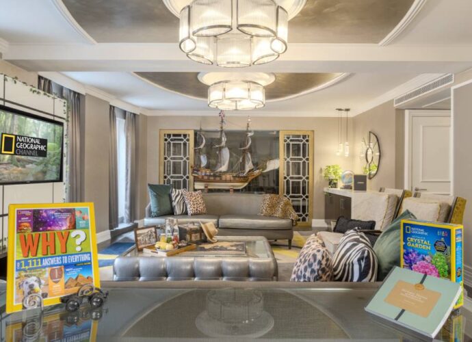 National Geographic themed hotel suite with a living area, ship model, patterned decor, and games displayed on a table.