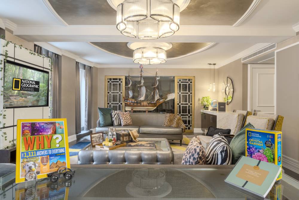 National Geographic themed hotel suite with a living area, ship model, patterned decor, and games displayed on a table.