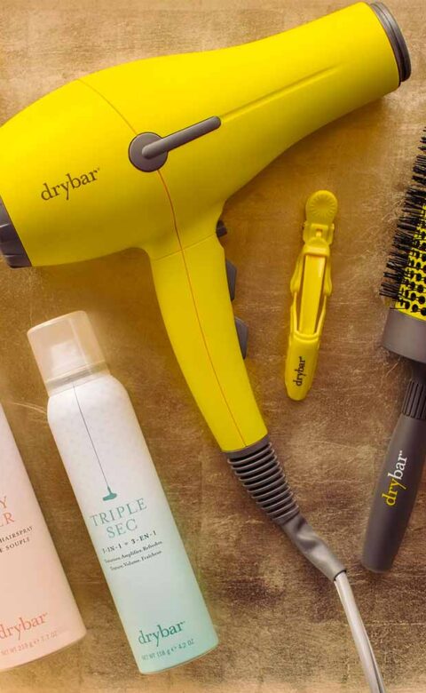 a Drybar hair dryer, brush, hair clips, and hair products laid out for display