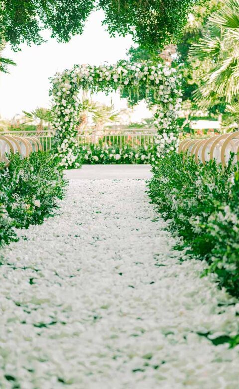 flower petal covered aisle leading to flower arch set for beautiful outdoor wedding venue