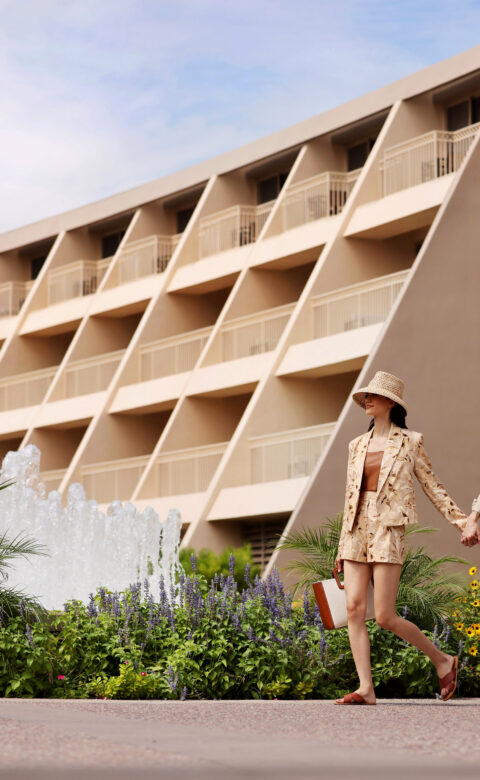 a man and a woman holding hands walking in front of a hotel