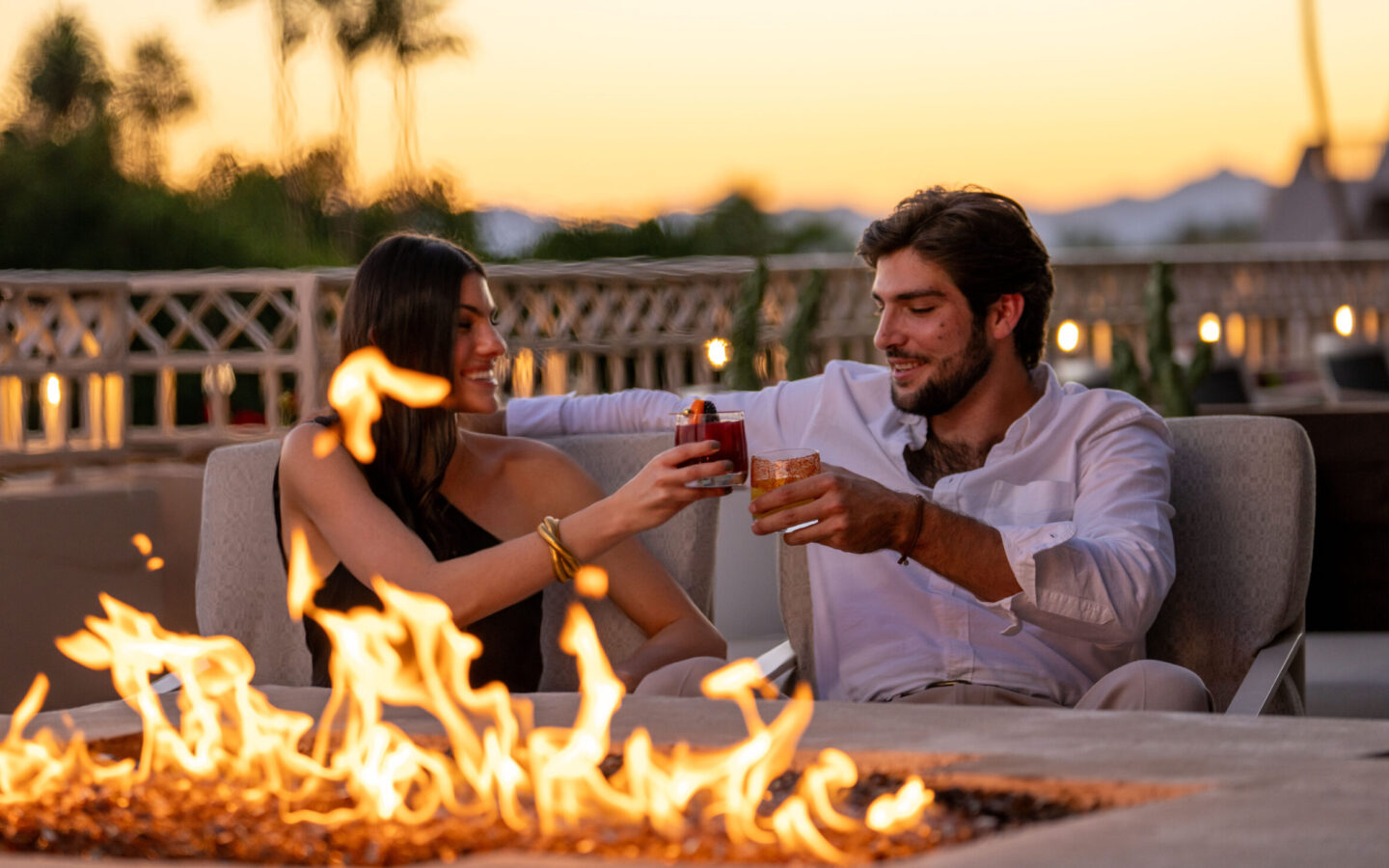 a man and a woman sitting next to each other in front of a fire pit