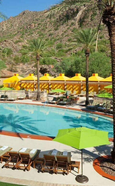 pool surrounded by lounge chairs palm trees and and yellow cabanas in the background