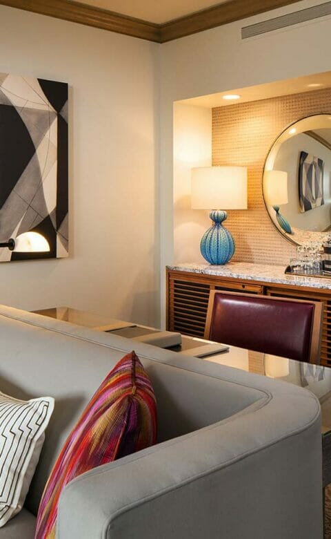 grey couch with two colorful red pillows and striped black and white pillow with desk art and circular mirror in the background