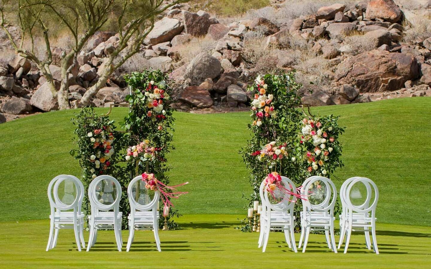 intimate wedding ceremony on lawn with large floral arch and white chairs