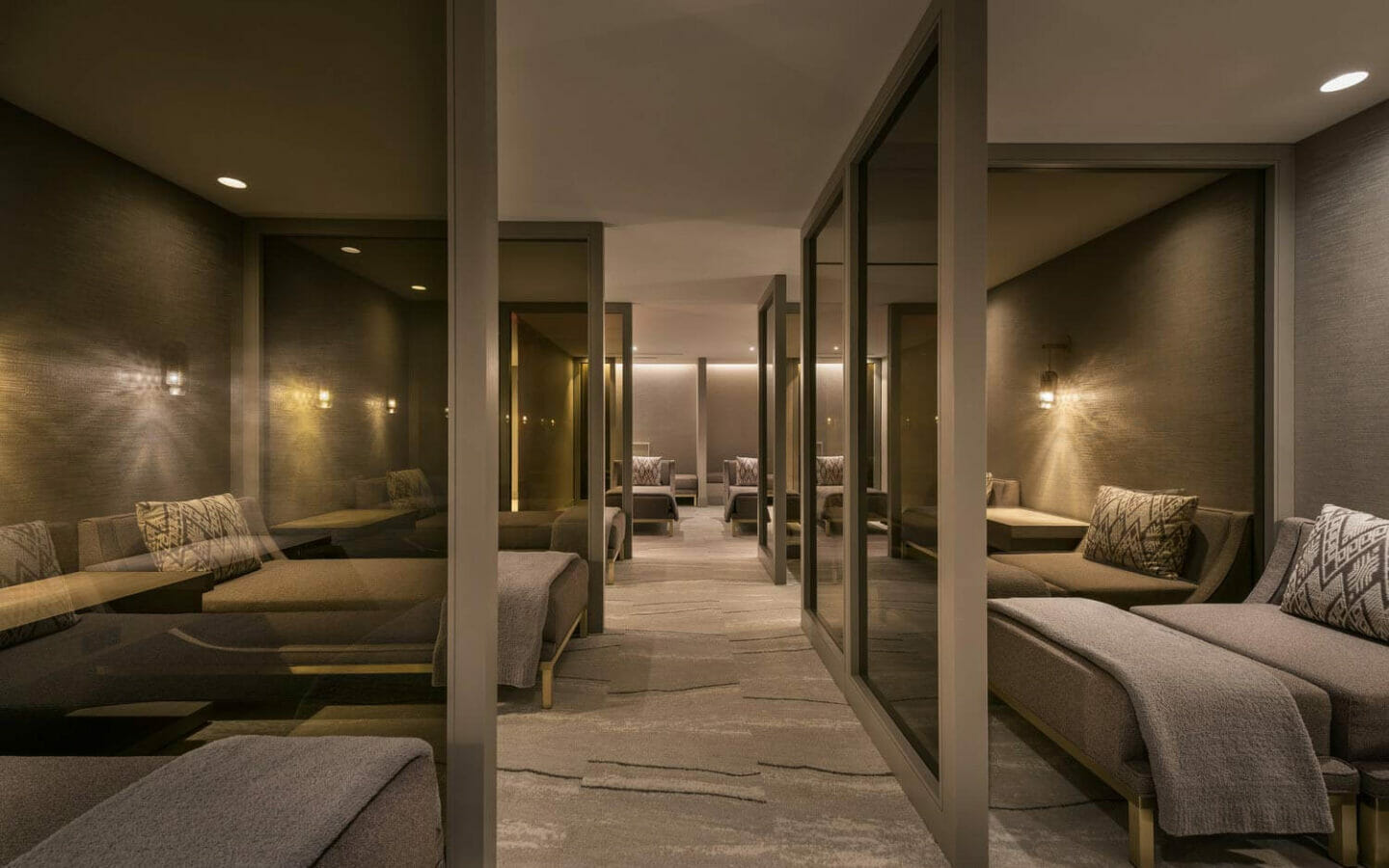 rows of daybeds, separated by glass panes, in a comfortable and dimly lit spa post-treatment room