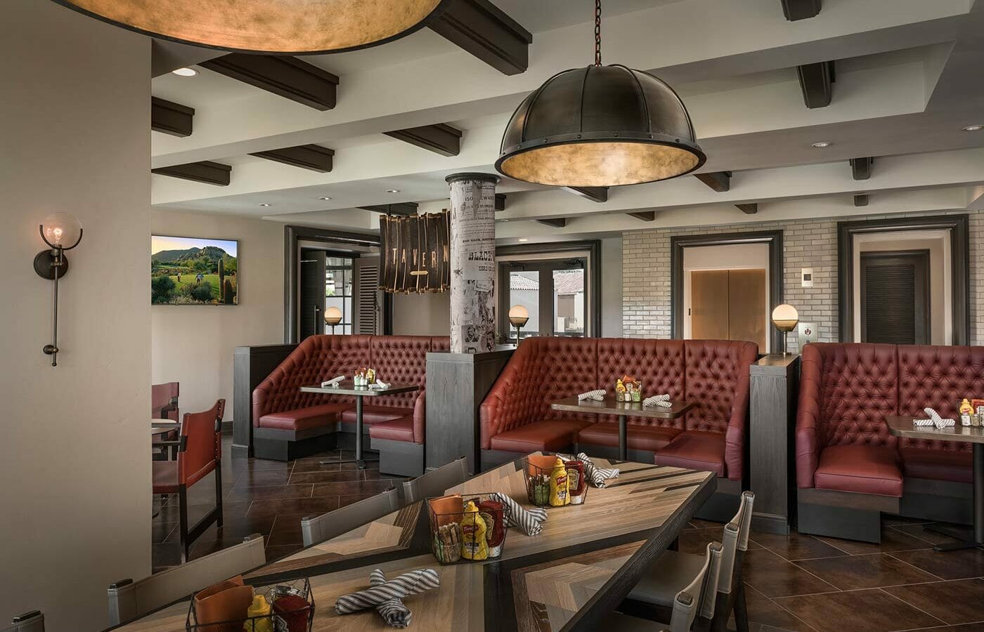 The Phoenician Tavern dining area with long striped table in the foreground and red leather booths in the background